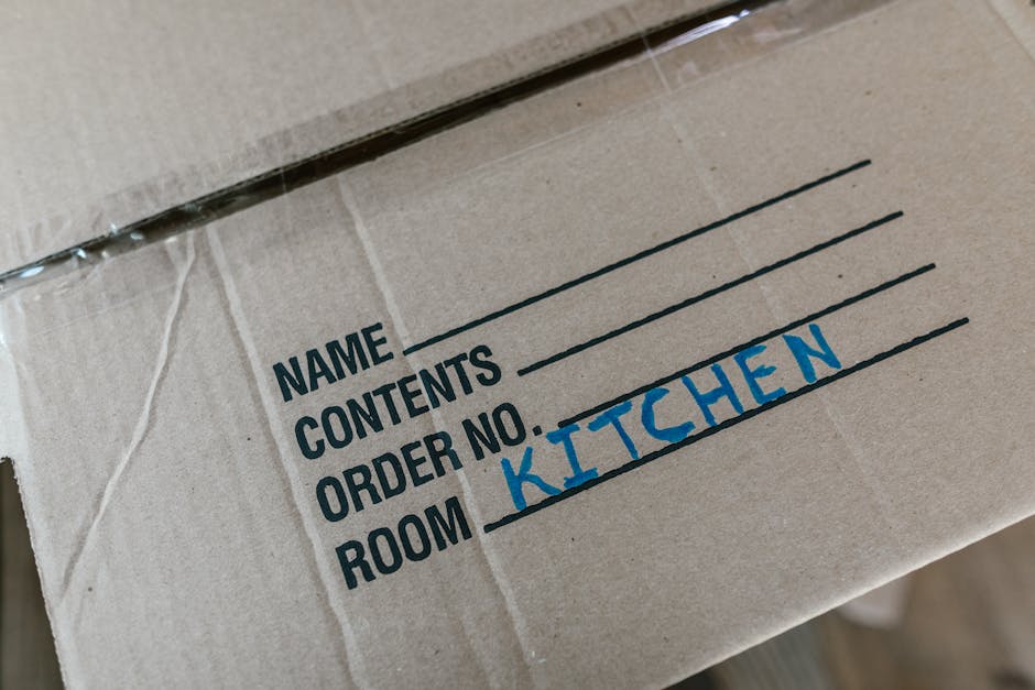 Two movers from [COMPANY_NAME] are loading a large piece of furniture wrapped in green moving blankets into the rear of a white commercial van during a home relocation in an outdoor urban setting. The